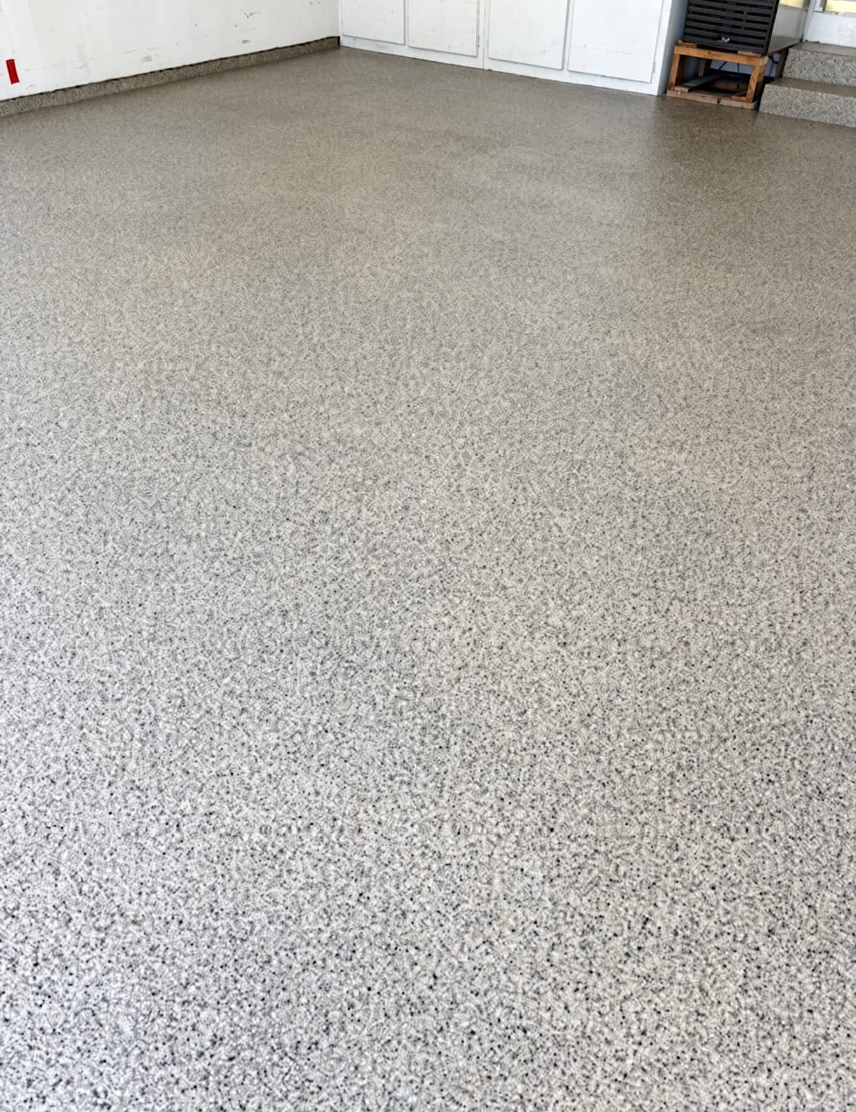 The same two-car garage after a full-flake coating — a grey and white flake finish laid seamlessly wall to wall and carried up the base of the walls.